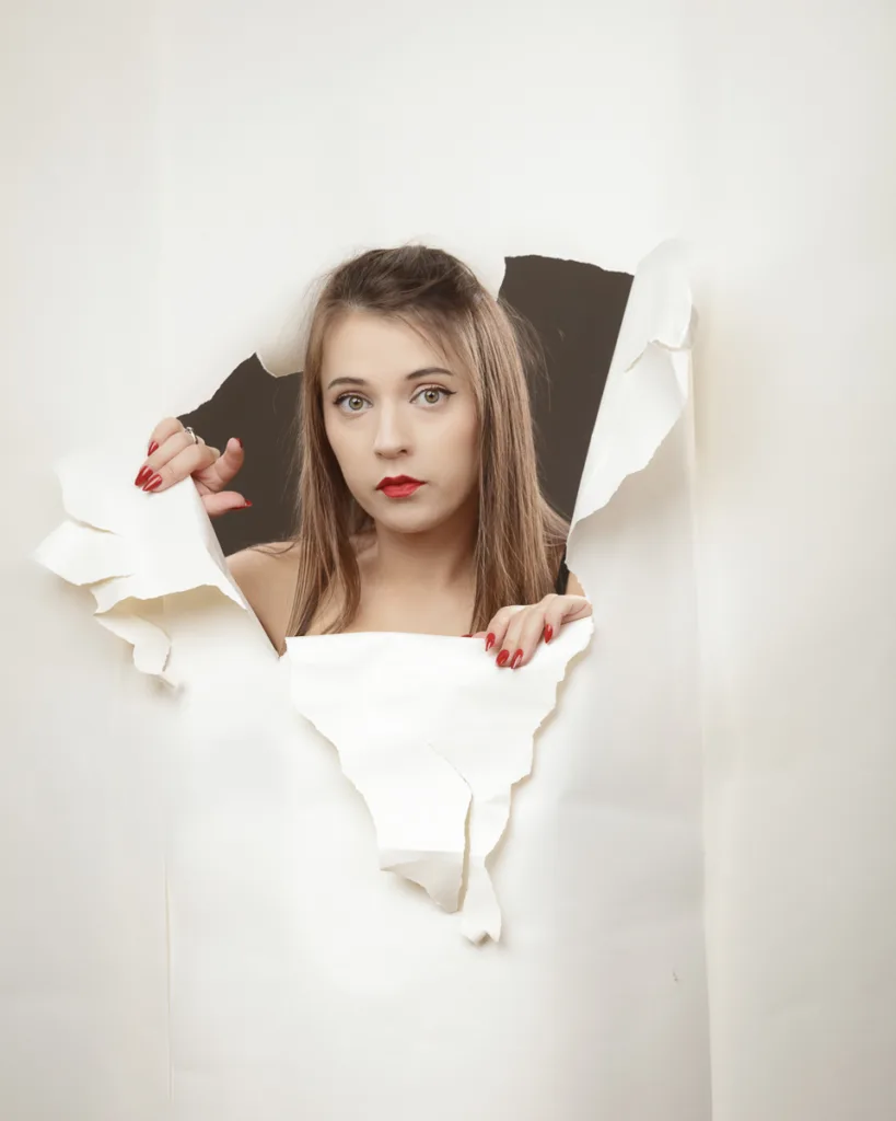 Person emerging through torn white paper background.