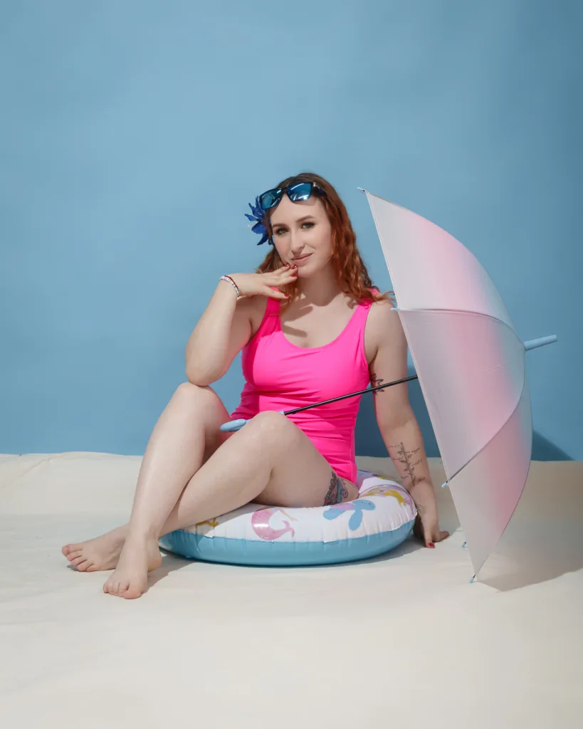 Woman in pink swimsuit with umbrella posing indoors