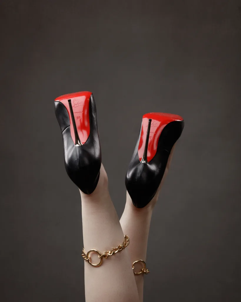 Red-soled black high heels on legs with bracelets.